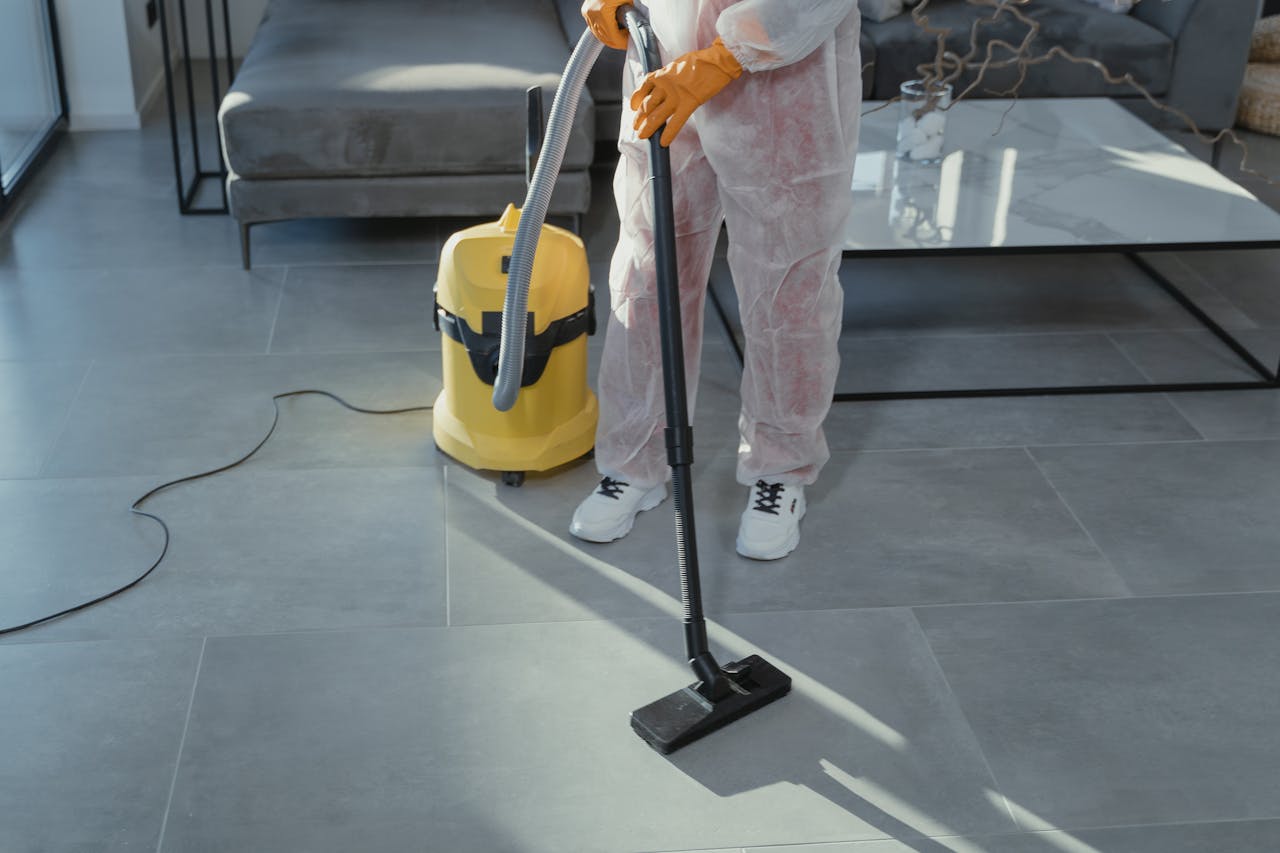 about-us A professional cleaner in protective gear vacuuming the floor in a modern living room.