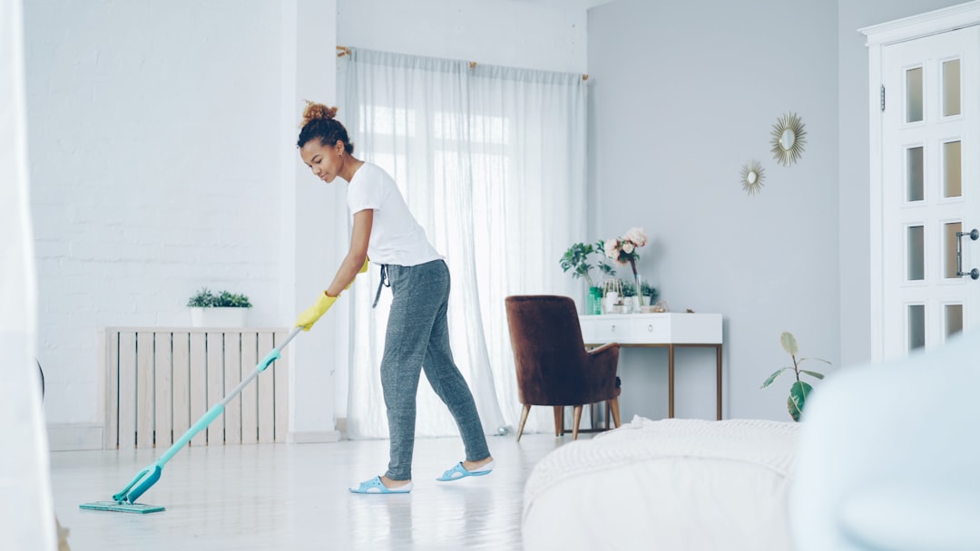 services-06 Pretty African American girl is mopping floor at home with flat plastic mop wearing gloves and wear-at-home clothing. Modern interiors, cleanness and young people concept.